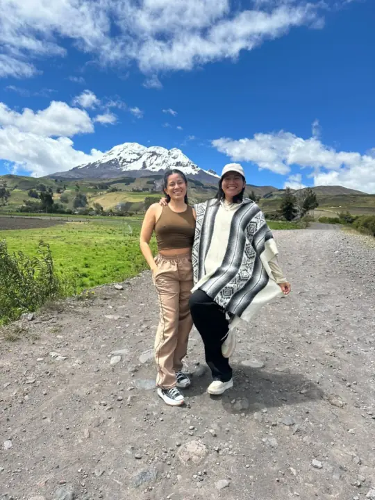 Two women on a dirt road with the snowy Chimborazo volcano behind them
