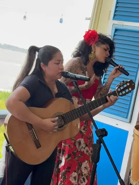 Two singers with a guitar and microphones performing in front of a blue wooden house