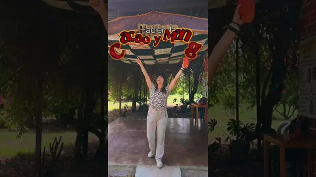 Video still: a woman with arms raised under a cacao farm sign